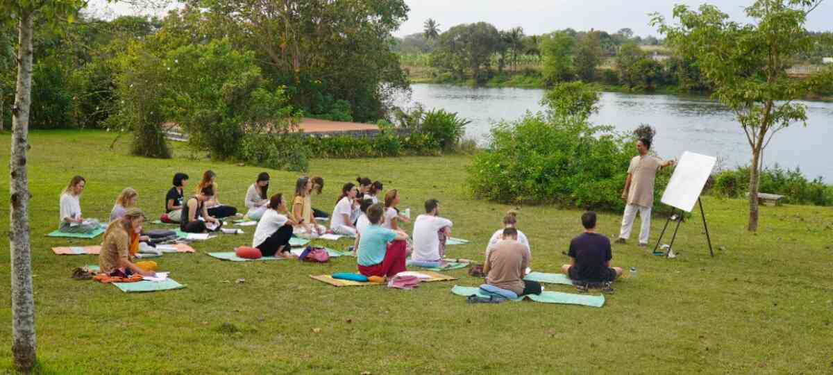 Intensive yoga retreat in India – students practising on the lawn by the river at the Mysore ashram